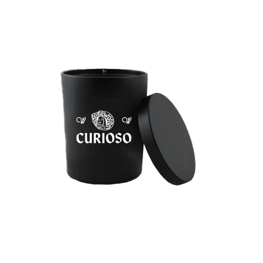 A black candle with a label that reads 'CURIOSO' and a lid on top, placed against a white background.